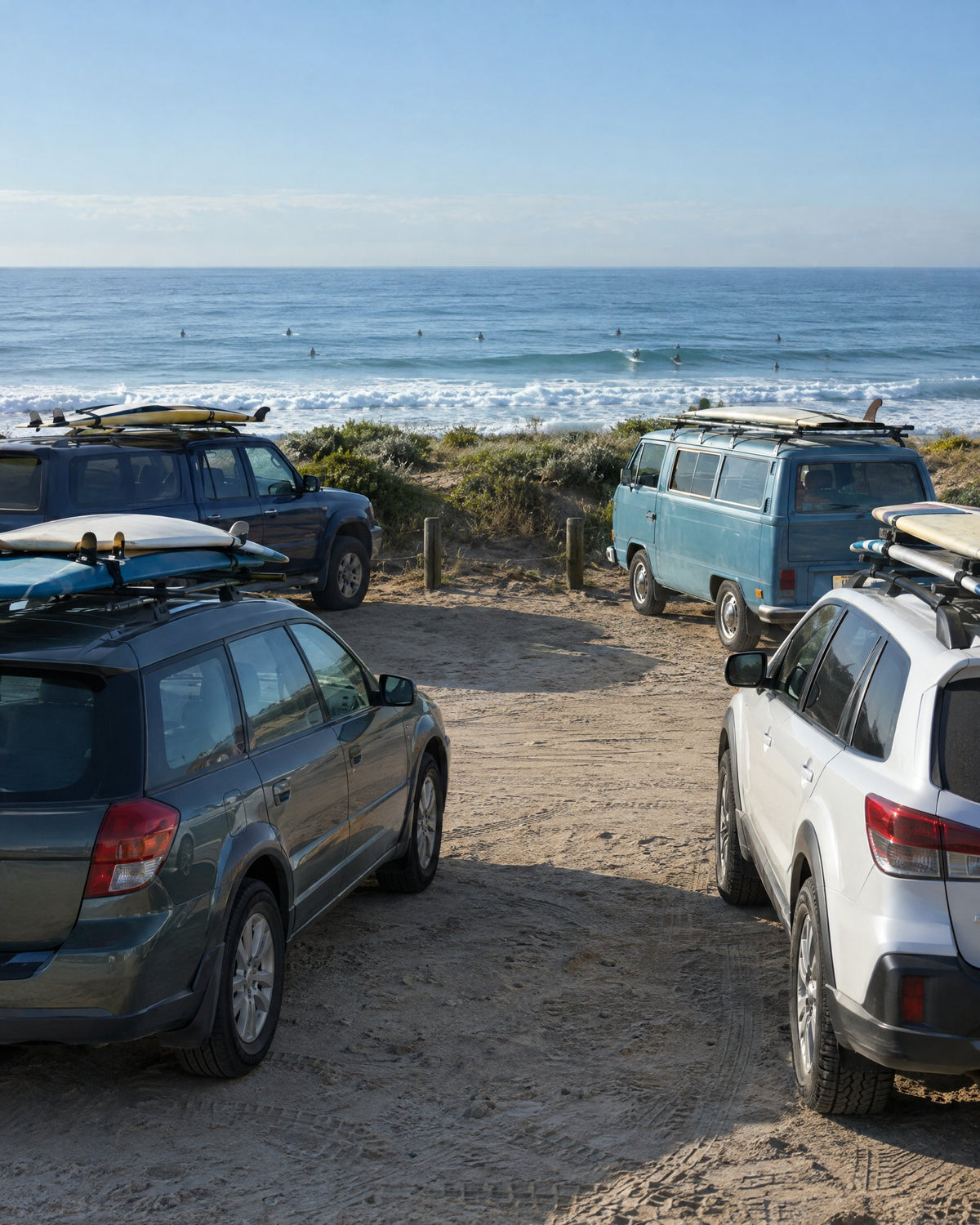 Cars with surfboards on their roofs parked in a sandy lot above the ocean