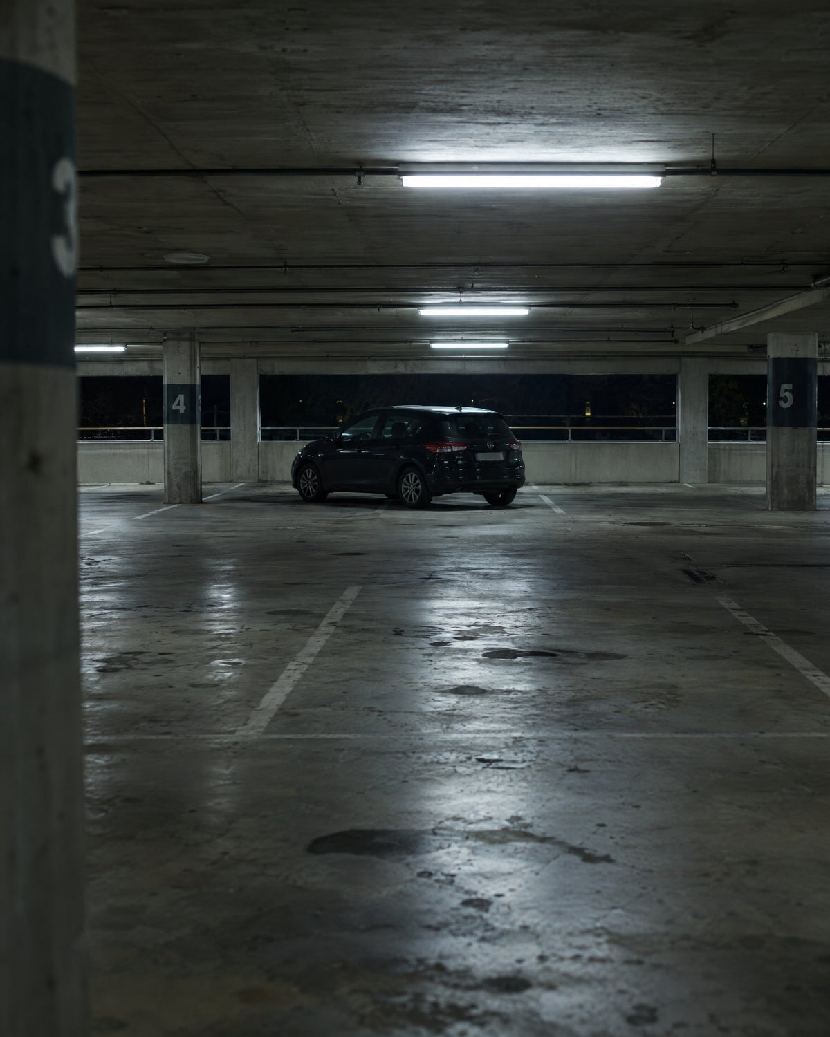 Lone hatchback parked in a dim, empty concrete parking garage