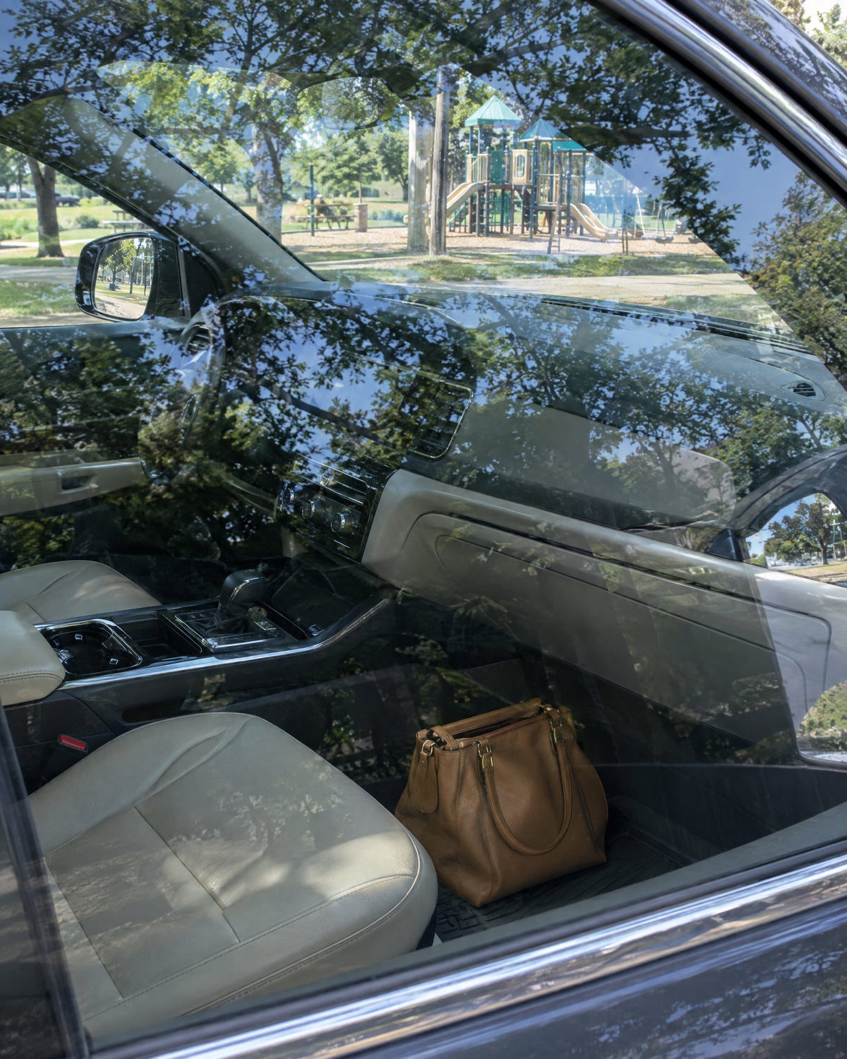 Brown purse on a car's passenger floor, seen through the window with a playground beyond